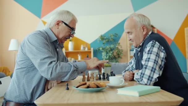 Evde satranç oynayan neşeli yaşlı adamlar masada birlikte oturarak konuşuyorlar. — Stok video