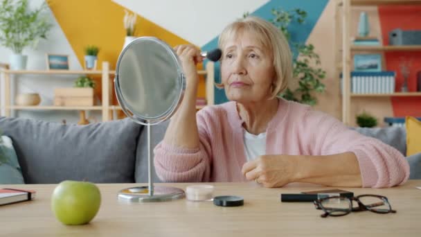 Медленное движение пожилой женщины, наносящей макияж с помощью косметики и зеркала дома — стоковое видео