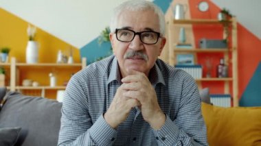 Gözlüklü sağlıklı yaşlı bir adamın portresi. Kanepede ciddi bir yüzle oturuyor. Sonra gülümsüyor.
