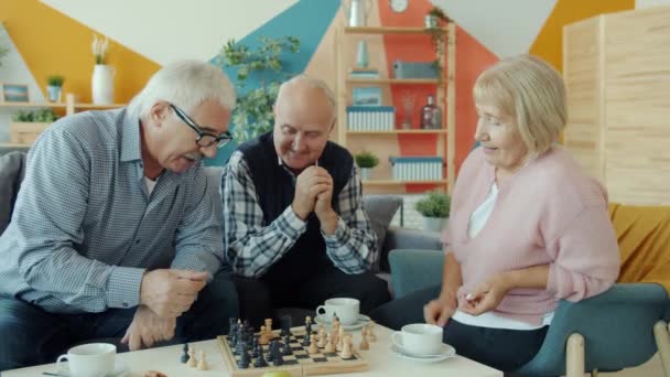 Oudere man en vrouw spelen schaak terwijl oudere man kijkt en lacht in appartement — Stockvideo