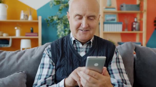Powolny ruch uśmiechniętego starszego mężczyzny smsującego za pomocą smartfona w domu — Wideo stockowe