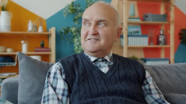 Портрет пенсионера в повседневной одежде, сидящего дома на диване и улыбающегося — стоковое видео