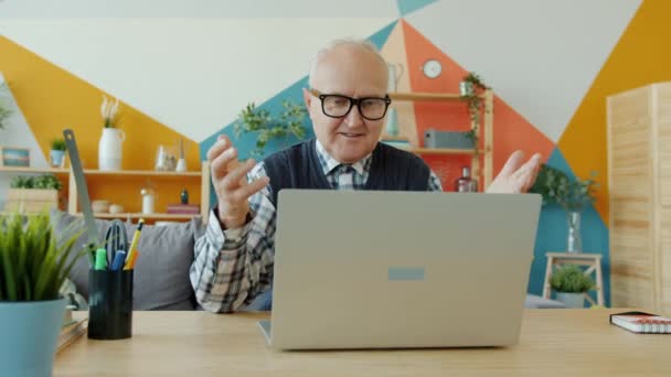 Cámara lenta de alegre anciano haciendo videollamada en línea con el ordenador portátil en casa — Vídeo de stock