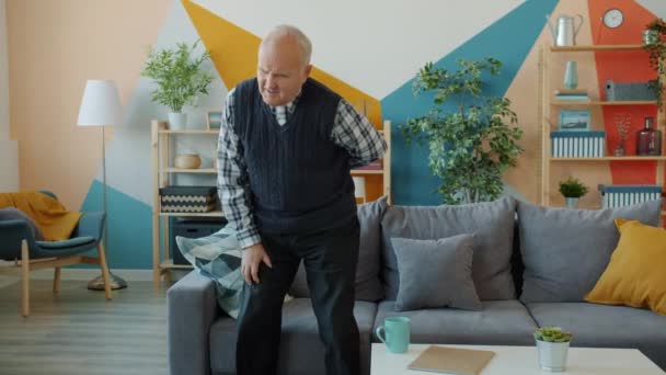 Нездоровый пожилой человек, страдающий от боли в спине, стоит в помещении в квартире — стоковое видео