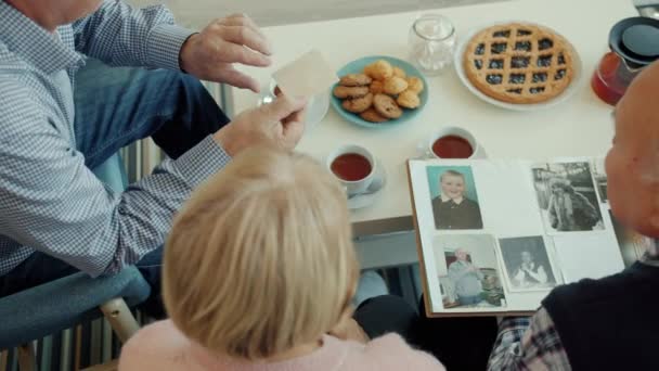 Back view of elderly people friends watching picture album talking holding photos — Stock Video