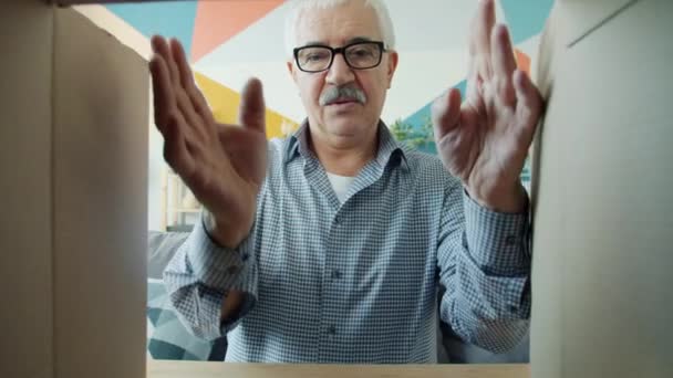 Portret van een gelukkige gepensioneerde man die een kartonnen doos opent met een vr-bril die thuis lacht — Stockvideo