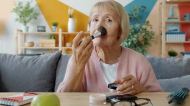 Makyaj yapan, saçlarını tarayan ve kameraya bakıp gülümseyen yaşlı güzel bir kadının portresi.