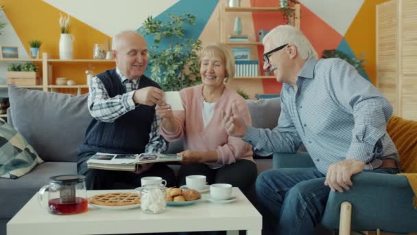 Old people friends watching photos talking sitting at table with food in apartment — Stock Video