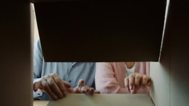 Homem sênior e mulher casal feliz abertura caixa de papelão olhando para dentro sorrindo em casa — Vídeo de Stock