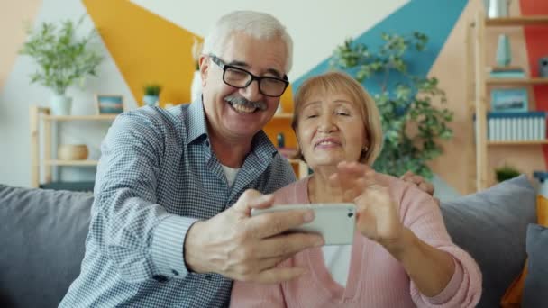 Rentner Mann und Frau machen Online-Videoanruf winkende Hand hält Smartphone zu Hause — Stockvideo