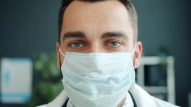 Hastane ofisinde maske takmış çekici genç bir doktorun vesikalığı.