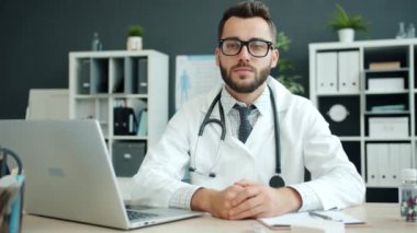 Klinikteki kameraya bakan üniformalı ve gözlüklü ciddi bir doktorun portresi.