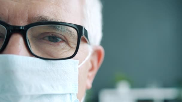 Крупный план портрета пожилого человека в очках врача в маске в помещении клиники — стоковое видео