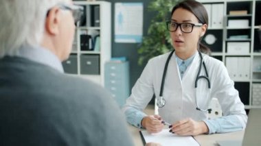 Genç kadın doktor ofiste yaşlı bir adamla el sıkışıyor.