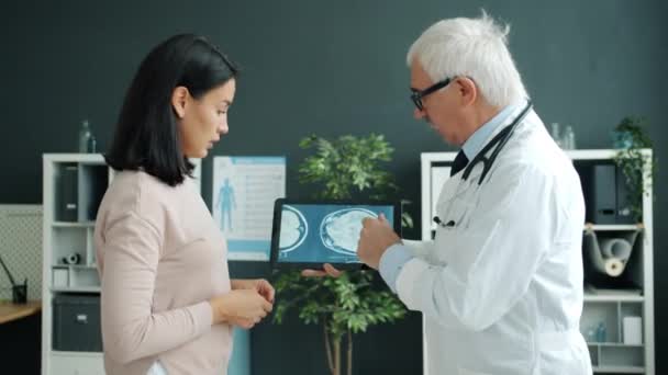 Médico mostrando imagens de ressonância magnética para paciente do sexo feminino usando tablet tocando tela trabalhando no escritório — Vídeo de Stock