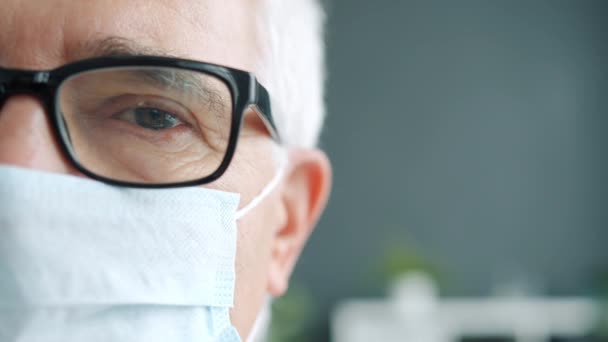Primer plano media cara retrato de hombre mayor en máscara médica y gafas mirando a la cámara — Vídeo de stock