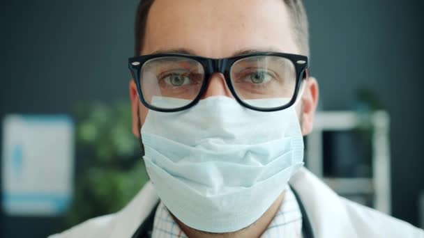 Close-up portret van arts jongeman met bril dragen masker binnen in het ziekenhuis — Stockvideo