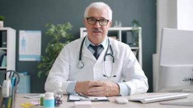 Gözlüklere dokunan deneyimli doktor portresi ciddi bir yüzle kameraya bakıyor.