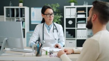 Dost canlısı bir doktor genç bir adamla konuşuyor ve hastane odasında çizelgeyi dolduruyor.