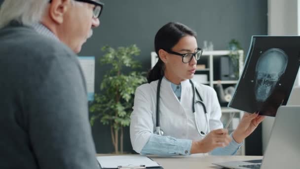 Alegre doctora hablando con paciente mayor mostrando resultados de rayos X en clínica — Vídeos de Stock