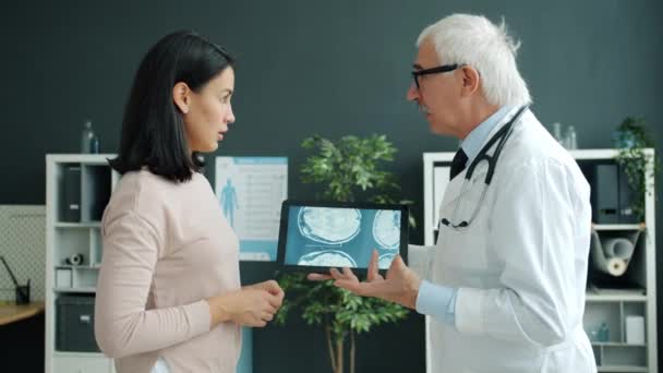 Врач и пациент обсуждают состояние здоровья глядя на снимки МРТ на экране планшета в офисе — стоковое видео