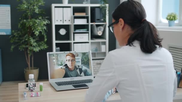 Medic jonge vrouw in uniform praten met zieke man online met behulp van computer van kliniek — Stockvideo