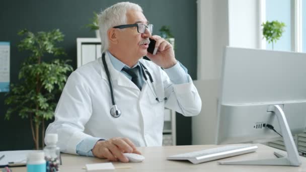 Médico especialista conversando com o paciente no telefone celular e usando PC trabalhando no escritório — Vídeo de Stock