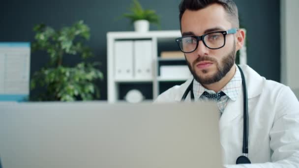 Guy médico usando portátil en la oficina se concentró en el trabajo con la computadora en el hospital — Vídeos de Stock