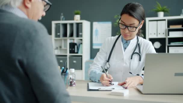 Médico femenino consultando paciente anciano en hospital hablando escrito en carta — Vídeos de Stock