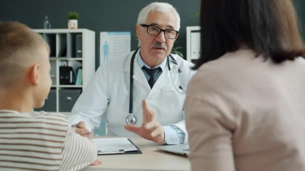 Médico sênior conversando com a família mãe e filho discutindo saúde infantil no escritório — Vídeo de Stock