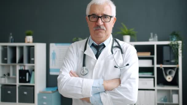 Портрет впевненого досвідченого лікаря, що стоїть в офісній кімнаті з схрещеними руками — стокове відео
