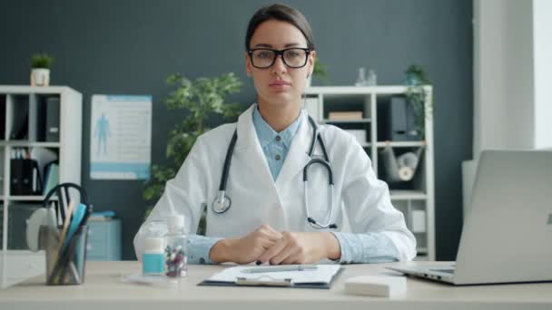 Ritratto di giovane donna seria medico alla scrivania in ufficio guardando la macchina fotografica — Video Stock