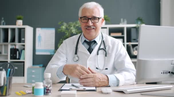 Veselý lékař starší muž dotýká brýle s úsměvem při pohledu do kamery na klinice — Stock video