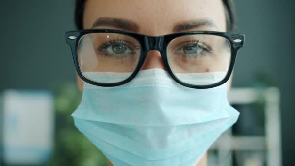 Gros plan d'une jolie femme médecin portant des lunettes et un masque médical à l'intérieur — Video