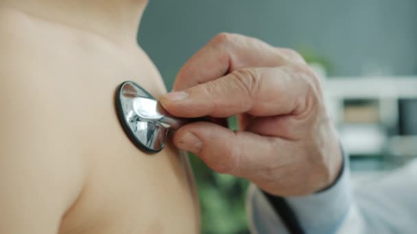 Ofisteki çocukların göğüslerini inceleyen steteskoplu doktorların yakın çekimi. — Stok video