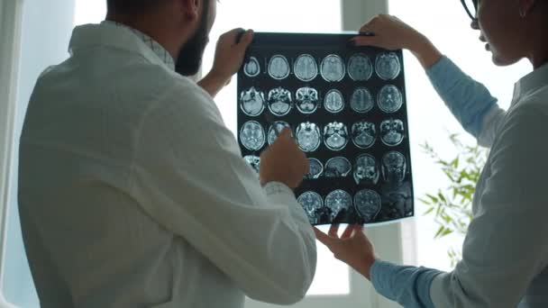 Médicos masculinos y femeninos sosteniendo y estudiando imágenes de resonancia magnética discutiendo caso en el hospital — Vídeo de stock