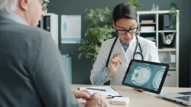 Señorita joven en uniforme blanco que muestra los resultados del examen de resonancia magnética del paciente en la pantalla del comprimido — Vídeo de stock