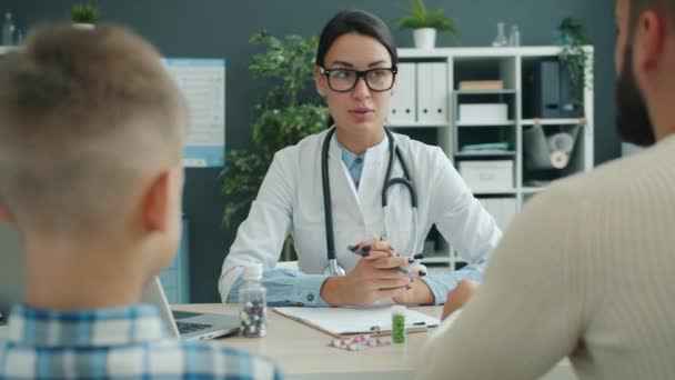 Lekarz dla dzieci rozmawia z ojcem i synem w klinice omawiając zdrowie dzieci — Wideo stockowe