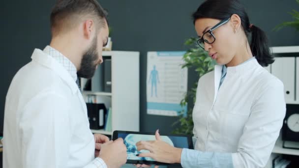 Médicos alegres hombre y mujer usando tableta en el trabajo hablando en la oficina — Vídeos de Stock