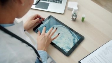 Genç kadın doktor, MRI görüntülerini tablet ekranda tek başına çalışırken inceliyor.
