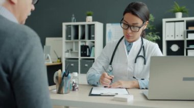Klinikteki randevu sırasında yaşlı bir hastayla konuşan kadın doktor.