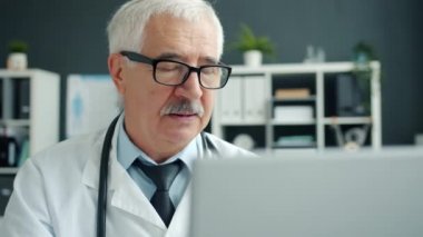 Ciddi bir doktor bilgisayar kullanıyor sonra da hastanede tek başına çalışan gözlüklere dokunuyor.