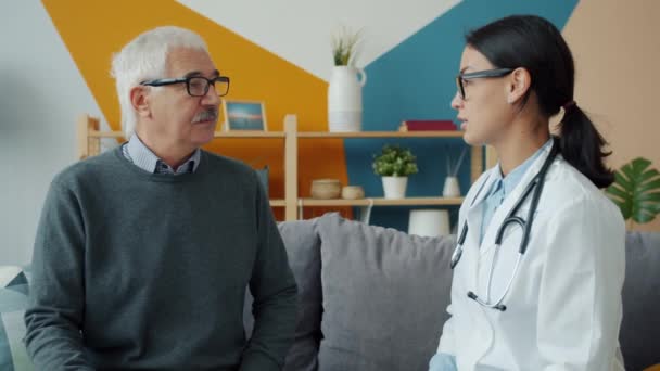 Doctora joven hablando con paciente mayor en casa expresando atención y apoyo — Vídeos de Stock
