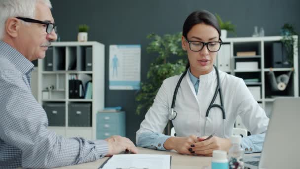 Zorgzame vrouwelijke arts in gesprek met oudere patiënt hand expressie van zorg in de kliniek — Stockvideo