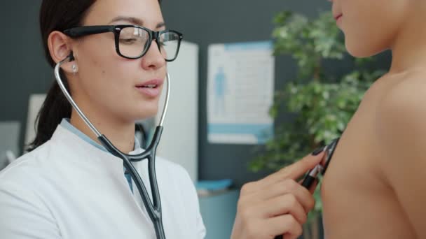女性の小児科医は、病院のオフィスで聴診器で呼吸する子供をチェック — ストック動画