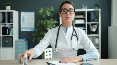 Hastane ofisinde gülümseyen ve hapları gösteren neşeli kadın doktor portresi.