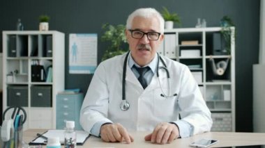 Neşeli doktorun portresi el sallayarak hastane ofisinde haplı şişeleri gösteriyor.