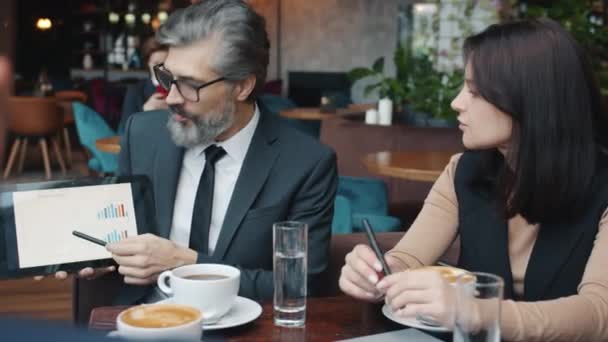 Rijpere zakenman toont grafiek op tablet scherm tijdens onderhandelingen in restaurant — Stockvideo