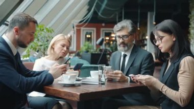 Bir grup iş adamı ve kadın, kafedeki masaya dokunarak akıllı telefonlar kullanıyor.