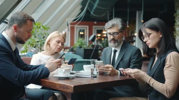 Grupo de hombres y mujeres de negocios que utilizan teléfonos inteligentes pantalla táctil en la mesa en la cafetería — Vídeo de stock